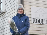 Eila Jouttunpää seisoo Koulumaan edessä ruusu kädessään.