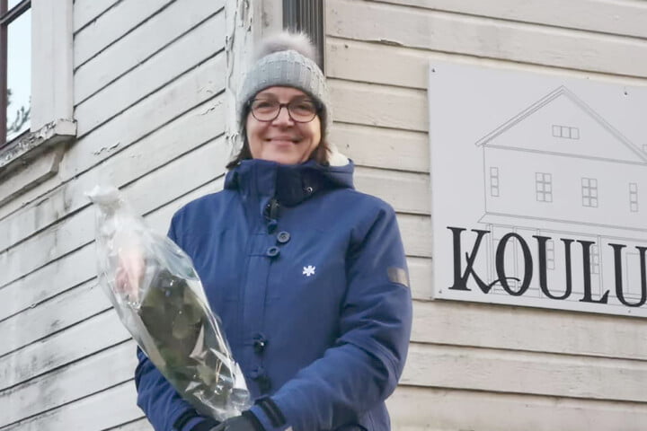 Eila Jouttunpää seisoo Koulumaan edessä ruusu kädessään.